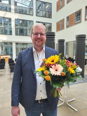 Pastor Simon Paschen lächelt glücklich mit Blumen in der Hand.