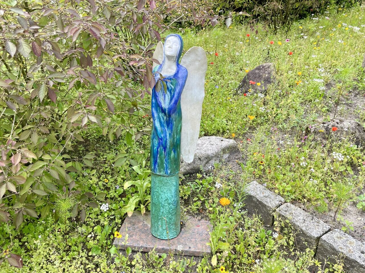 Engel in Form einer Figur aus Ton steht im Blumenbeet und hält sein Gesicht in die Sonne. Krankenhaus Reinbek St. Adolf-Stift